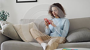 Happy hispanic teen girl holding cell phone using smartphone at home.