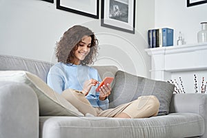Happy hispanic teen girl holding cell phone using smartphone at home.