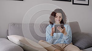 Happy hispanic teen girl using digital tablet sitting on couch at home.