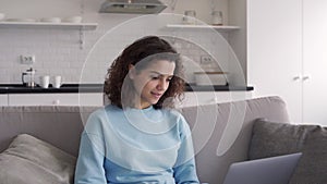 Happy hispanic teen girl using laptop computer sitting on sofa at home.