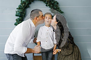 Happy holiday Christmas and New Year. Parents kiss their four-year-old son on the cheeks, and he is surprised