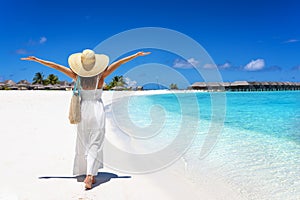 A happy holiday woman in a white dress walks down a tropical beach