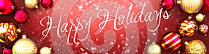 Happy holidays and Christmas card, red background with Christmas ornament balls, snow and a fancy and elegant word Happy holidays