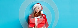 Happy holidays and Christmas concept. Cute redhead girl holding presents and pucker lips for kiss, wearing santa hat and