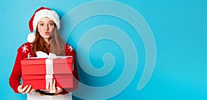 Happy holidays and Christmas concept. Cute redhead girl holding presents and pucker lips for kiss, wearing santa hat and