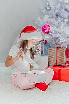 Happy holidays Cute little child opening present near Christmas tree. The girl laughing and enjoying the gift.