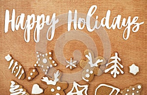 Happy holidays Greeting card. Happy holidays text handwritten on christmas gingerbread cookies on wooden background, flat lay.