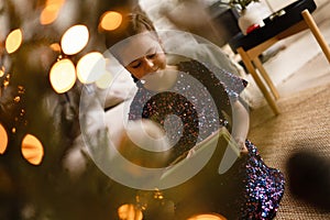 Happy holidays. Little child opening present near Christmas tree. The girl laughing and enjoying the gift.