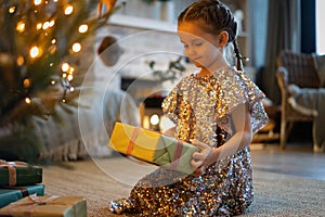 Happy holidays. Little child opening present near Christmas tree. The girl laughing and enjoying the gift.