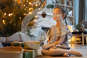 Happy holidays. Little child opening present near Christmas tree. The girl laughing and enjoying the gift.