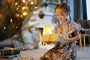 Happy holidays. Little child opening present near Christmas tree. The girl laughing and enjoying the gift.