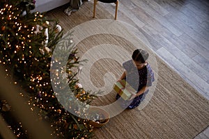 Happy holidays. Little child opening present near Christmas tree. The girl laughing and enjoying the gift.