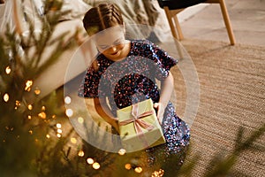 Happy holidays. Little child opening present near Christmas tree. The girl laughing and enjoying the gift.