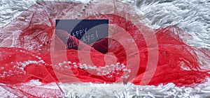 Happy holidays text on black card with red tulle and beads on white fluffy background