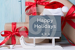 Happy Holidays text, Christmas gift boxes and santa hat, wooden background