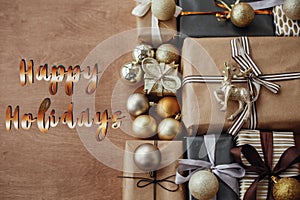 Happy Holidays text, handwritten golden sign at christmas stylish gift boxes with glitter tree and ornaments on rustic wooden