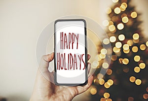 Happy Holidays text on phone screen on background of golden beau