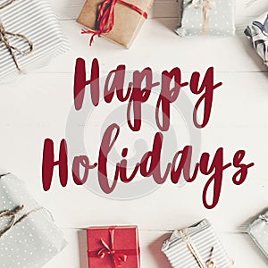 happy holidays text, seasonal greetings card sign. wrapped present boxes on white wooden background top view, flat lay.