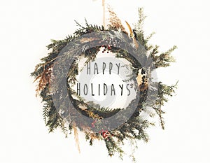 Happy Holidays text sign on  christmas rustic wreath. Creative rural  wreath with fir branches, berries, pine cones, herbs hanging