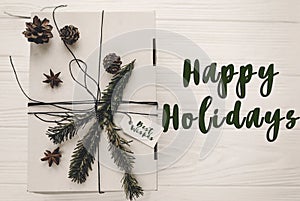 happy holidays text sign, greeting card. stylish christmas rustic gift box flat lay. white present with green tree fir branch and