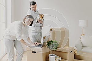 Happy home buyers pose near unpacked boxes, enjoy relocation in new house, woman searches ideas for redecoration bedroom, man photo