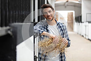 Happy horse farmer holding hay in stable