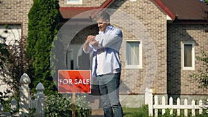 Happy house owner installing for sale signboard in front of building, moving