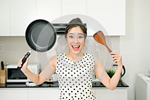 Happy housewife hold up with pan wooden turner in kitchen