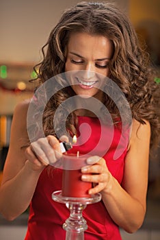 Happy housewife lighting red candle in kitchen