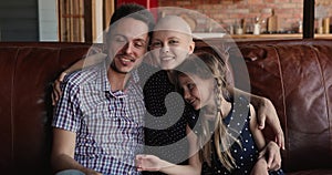 Happy husband, little daughter hugging smiling female cancer patient