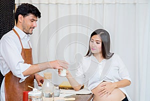 Happy husband and pregnant wife in kitchen,Asian man cooking food in kitchen and woman with drink milk at home