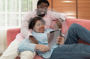 Happy husband and wife relaxing on couch in living room watching funny video on tablet together at home