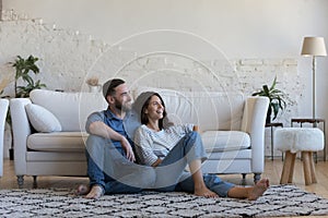 Happy husband and wife sitting close on heating carpeted floor