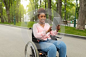 Happy impaired young woman in wheelchair using tablet computer for online communication outdoors