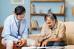 Happy indian banker taking sign from senior man at home - concept of loan approval, financial support and retirement