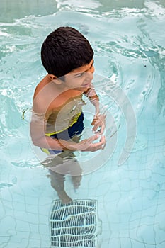 Happy Indian boy swimming in a pool, Kid wearing swimming costume along with air tube during hot summer vacations, Children boy in
