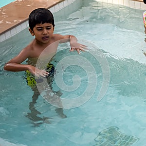 Happy Indian boy swimming in a pool, Kid wearing swimming costume along with air tube during hot summer vacations, Children boy in