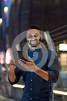 Happy indian business man using digital tablet outdoor in night city, vertical.