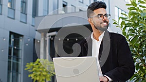 Happy Indian businessman typing working remote on wireless laptop computer browsing online outdoors