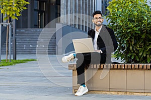 Happy Indian businessman typing working remote on wireless laptop computer browsing online outdoors