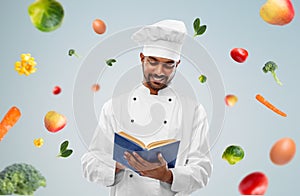 Happy indian chef reading cookbook over vegetables