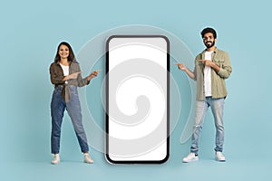 Happy indian couple pointing at big cell phone, mockup