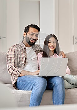 Happy indian dad with teenage daughter having fun using laptop at home.