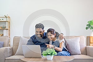 Happy indian family couple using laptop looking at computer laptop sitting on sofa together relaxing at home