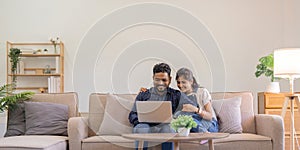 Happy indian family couple using laptop looking at computer laptop sitting on sofa together relaxing at home