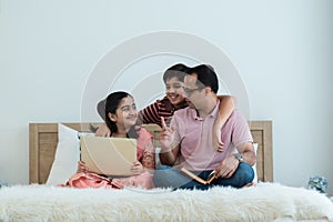 Happy indian family teenage boy son and girl with dad talking, teaching and doing daughter homework on laptop together at home