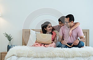 Happy indian family teenage boy son and girl with dad talking, teaching and doing daughter homework on laptop together at home