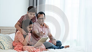 Happy indian family teenage boy son and girl with dad talking, teaching and doing daughter homework on laptop together at home