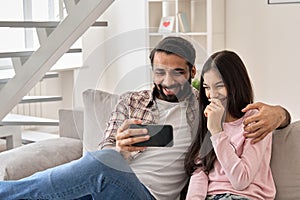 Happy indian father with teenage daughter having fun using phone at home.