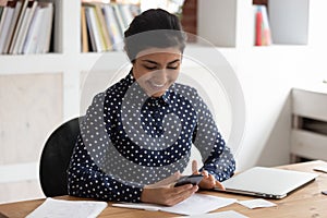 Smiling indian girl distracted from studying using cellphone